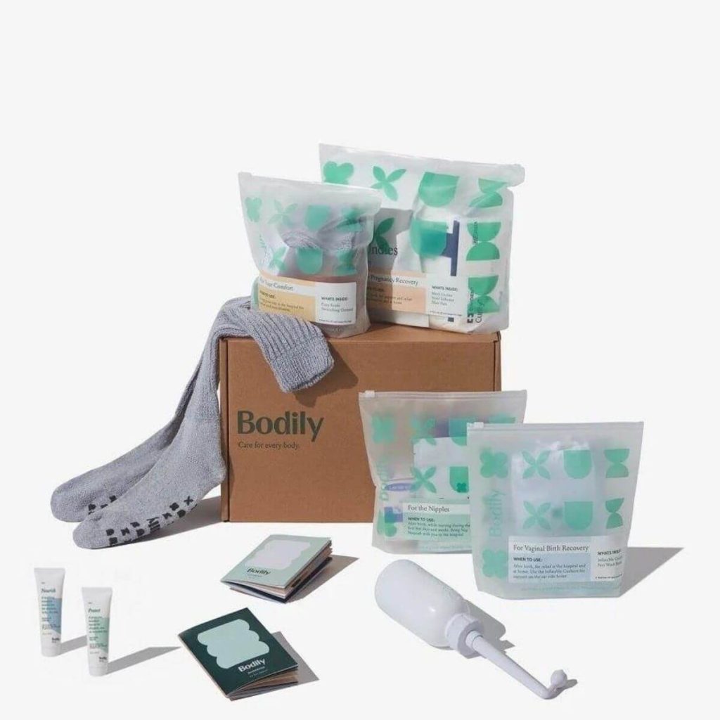 A brown box with the company name Bodily is sitting on a white table with grey socks and other postpartum essentials
