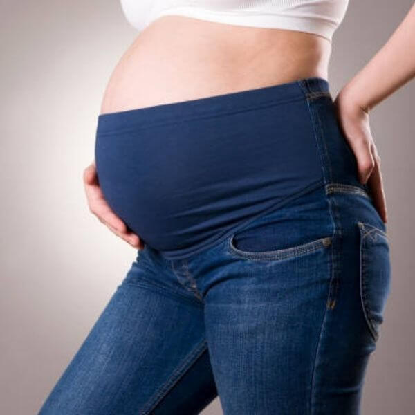 The bottom half of a woman is shown. She is pregnant and in dark blue jeans