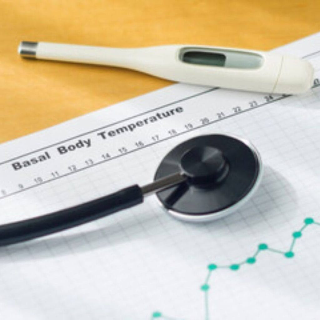 A light wood table has a thermometer, stethescope and a chart with Basal Body Temperature at the top