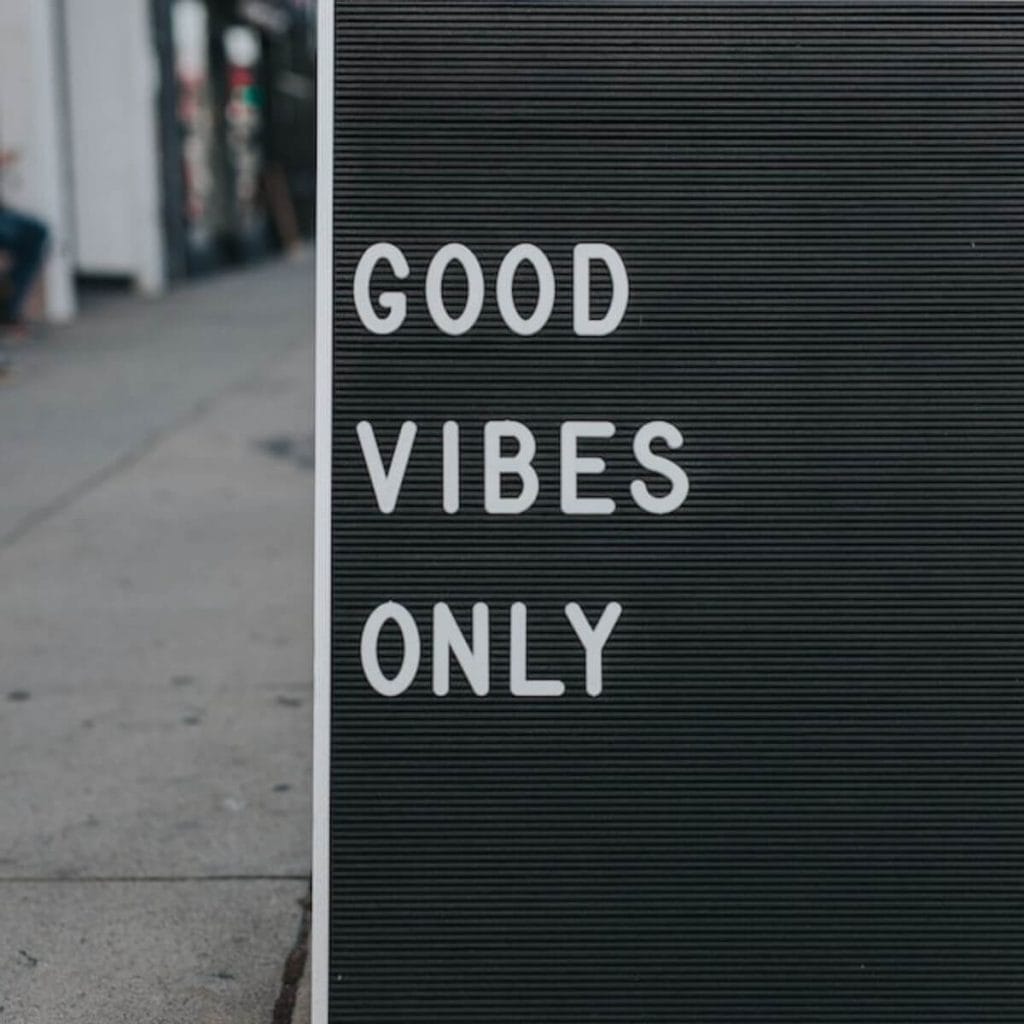 On a sidewalk is a black and white sign that says "Good Vibes Only".