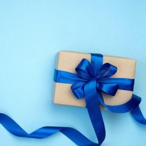 On a light blue table sits a tan colored box. It is wrapped in dark blue ribbon with a big dark blue bow on top.