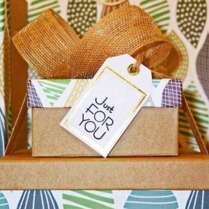 There is a small box stacked on top of a big box. They are wrapped in a gold colored gingham bow. The tag is white and reads "Just for you" in dark blue