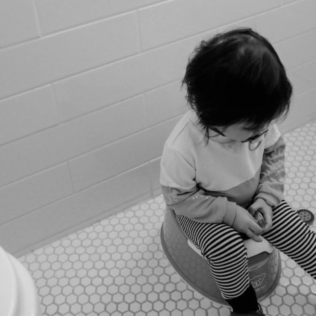 A child is sitting on a toddler potty in a bathroom with striped leggings on
