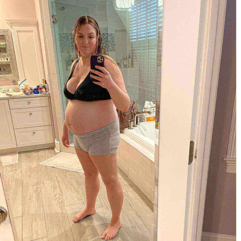 Katy is standing in her bathroom in a black nursing bra and grey Friday mom postpartum underwear.