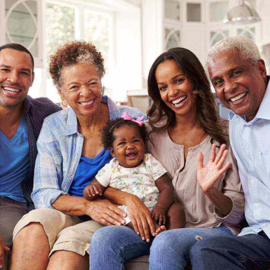 A multi-generational family is sitting on the couch smiling.