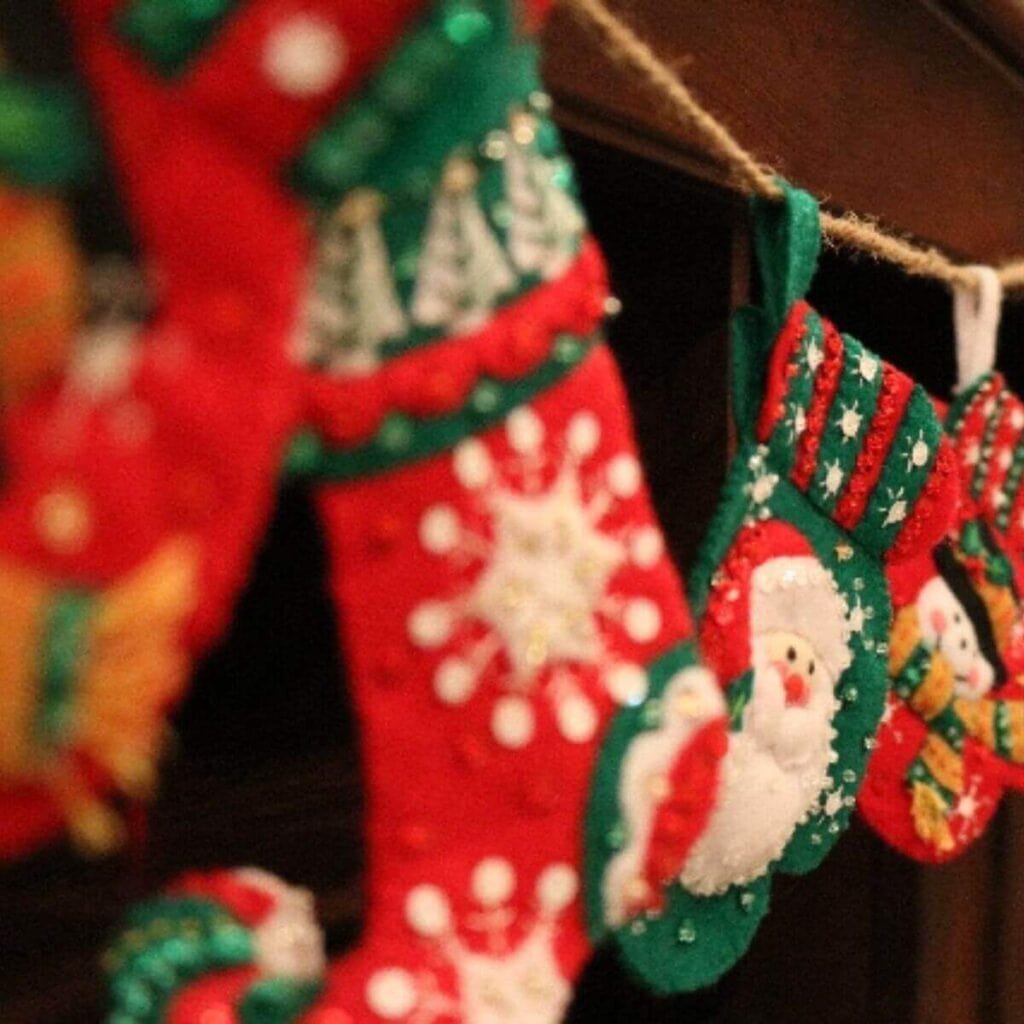 In front of a fireplace hangs four stockings from a rope. Three are red and the other is green.