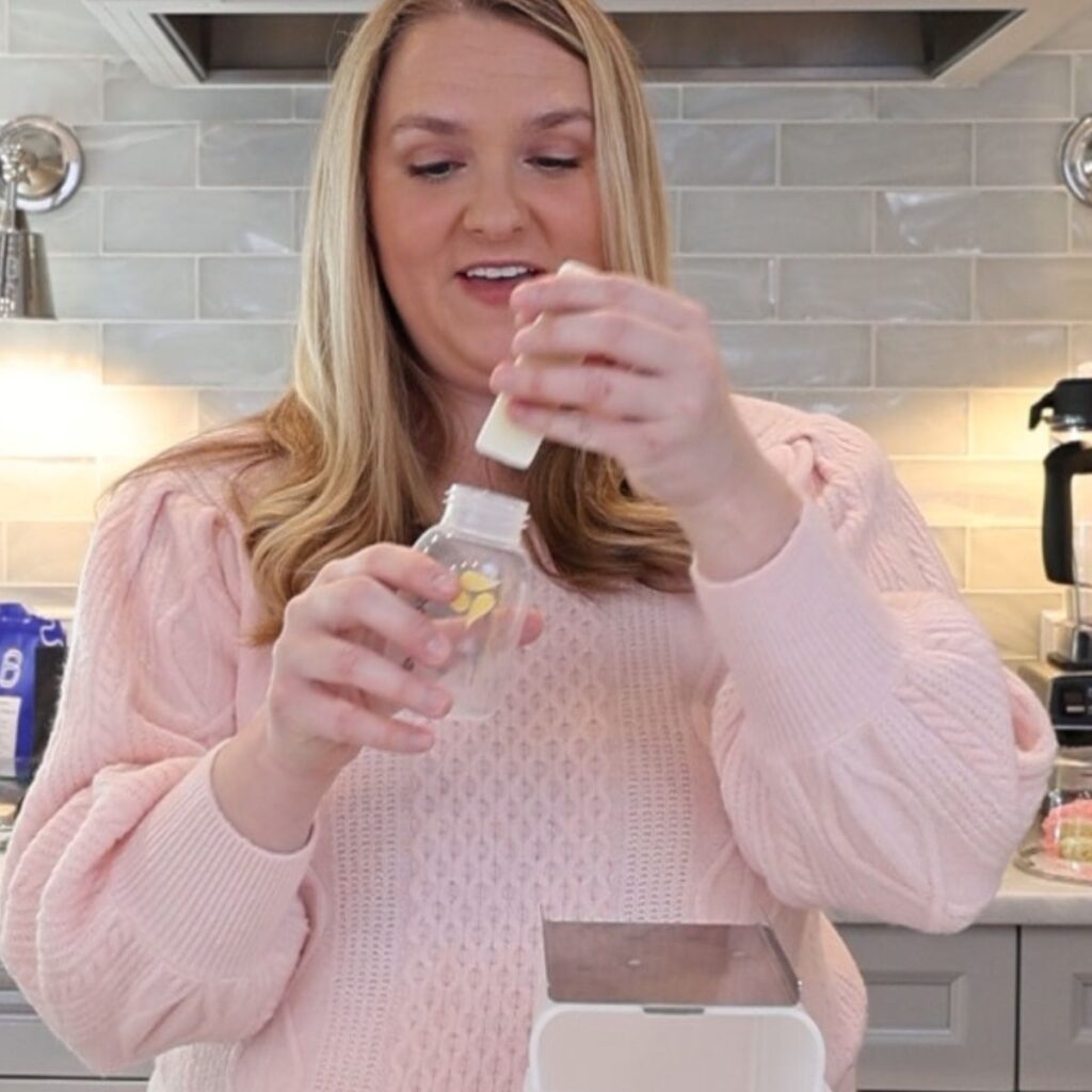 A woman puts a small stick of frozen breast milk into a bottle with a small, round mouth