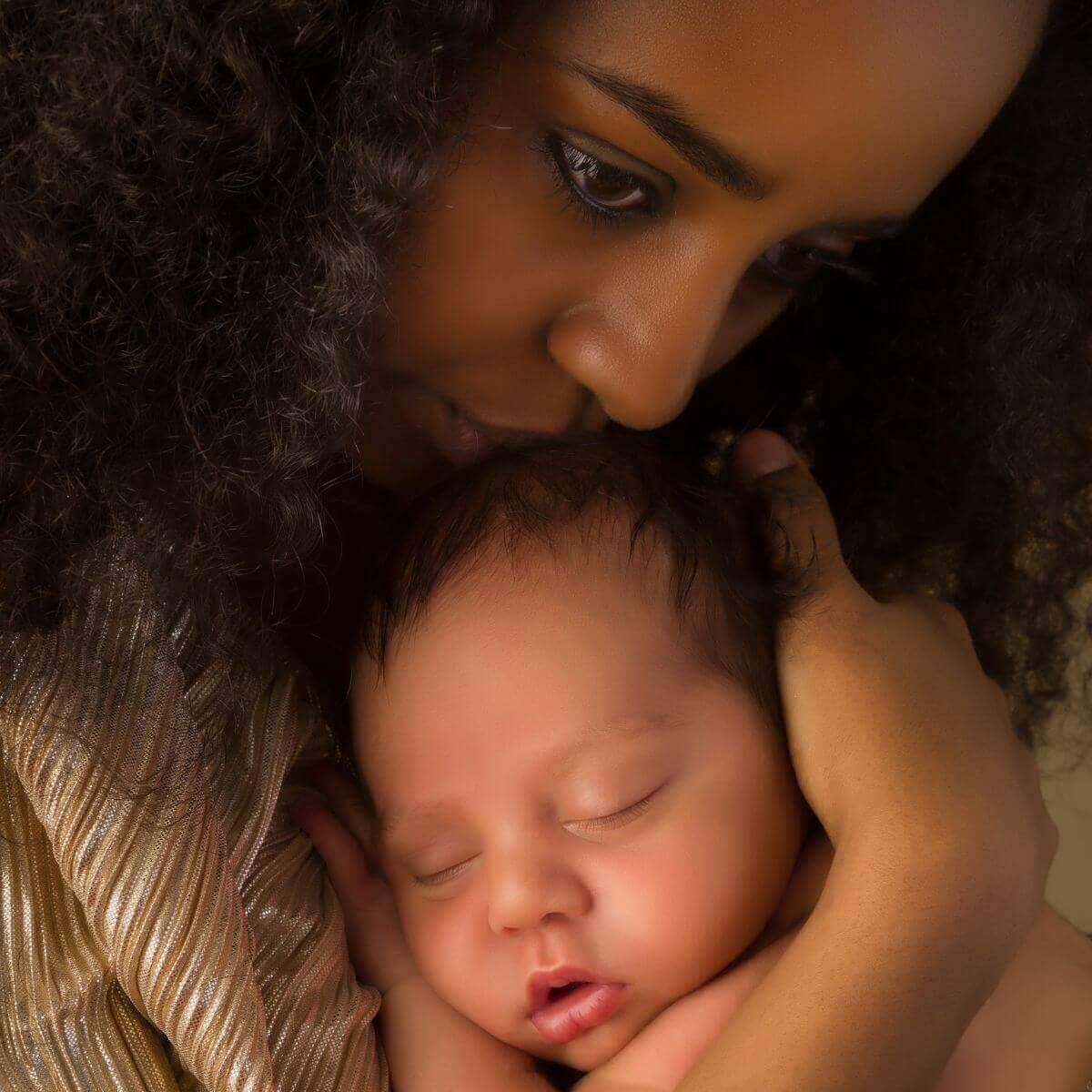 An African American woman is holding a newborn in her arms and she's staring down with a blank look on her face.