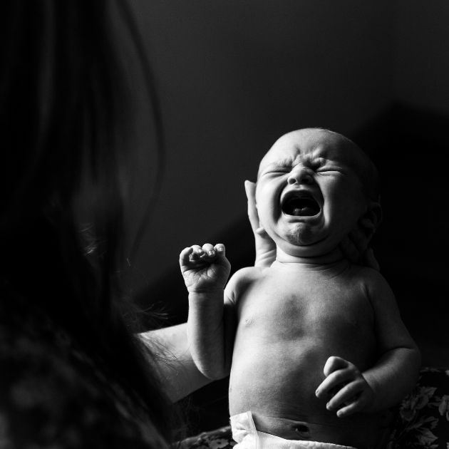 A black and white photo of a woman holding a crying baby wearing just a diaper.