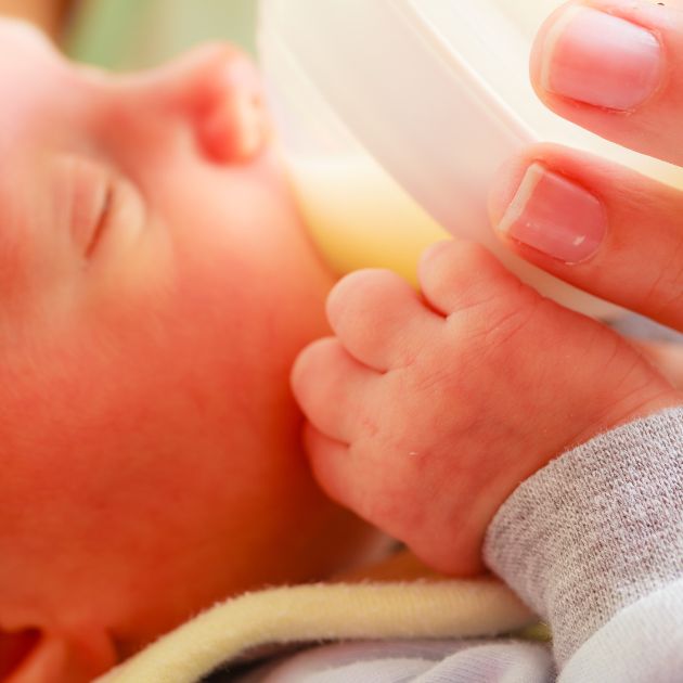 A baby with their eyes closed is being held while fed a bottle.