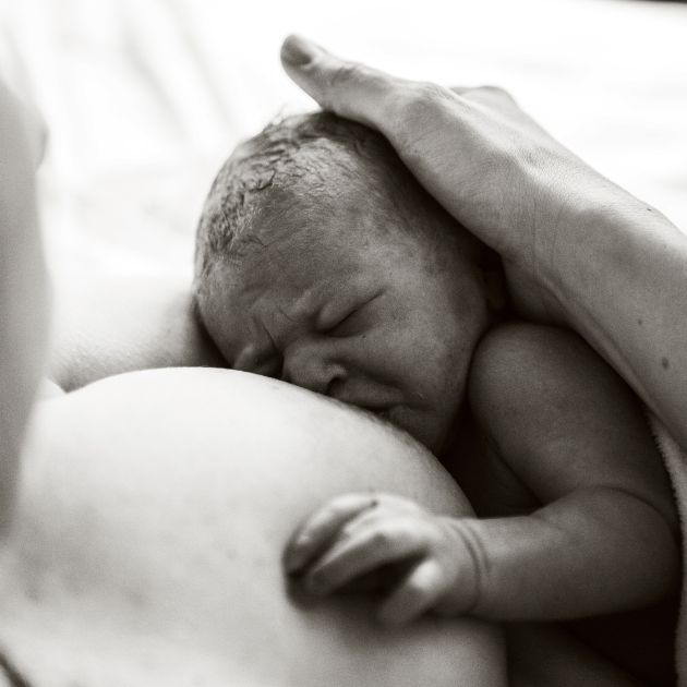 A black and white photo of a newborn breastfeeding while the mom cradles the baby's head.