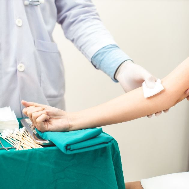 A woman's arm is stretched out on a medical table. A doctor's hand is holding gauze in the bend of her arm.