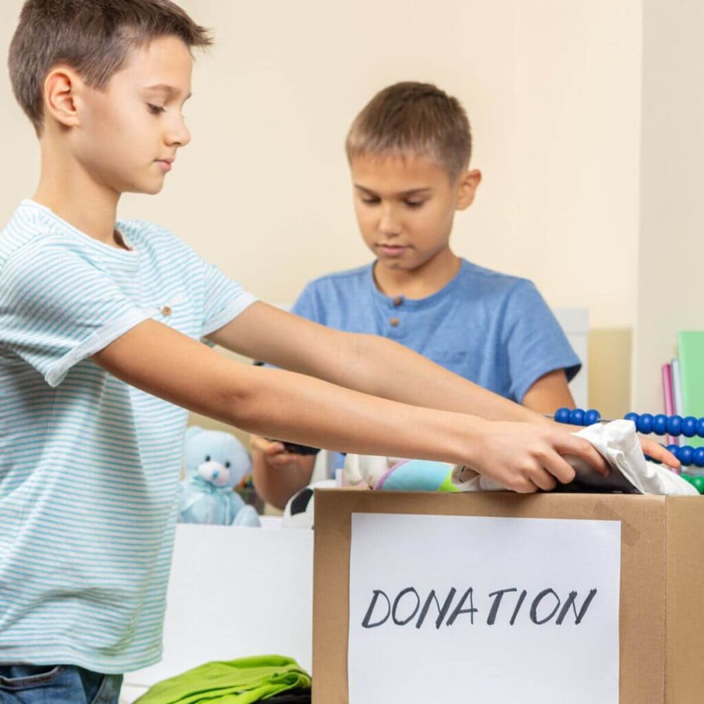 Two young boys put toys into a cardboard box with a paper taped to the box that says donation