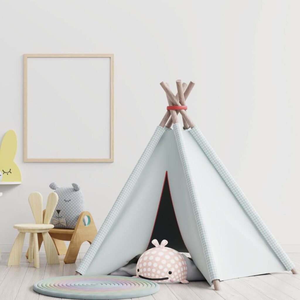 This square photo shows the corner of a playroom with a small soft blue teepee, with a stuffed snail peeking out from inside. There's a table with chairs next to the teepee with stuffed animals sitting in the child's-sized chairs, and a blank dry erase board on the wall.