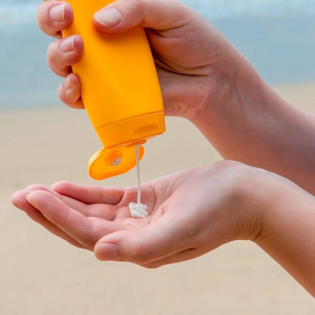 A woman has her left hand open in front of her. In her right hand is a yellowish orange tube of sunscreen and she is squeezing it into her left hand.