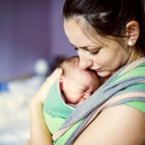 A woman is cradling her baby in a sling that is blue, dark green, light green, and pink.