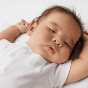 This photo is of a sleeping baby with its arms up by its head. The baby is sleeping peacefully.