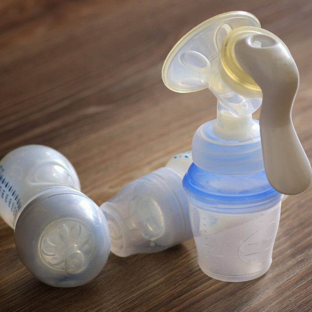 On a wooden table sits two empty bottles sitting on their sides and a bottle attached to a manual breast pump.