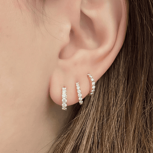 Image of woman wearing 3 diamond pave huggie earrings. They have 0.38ctw of diamonds and are set in yellow gold.