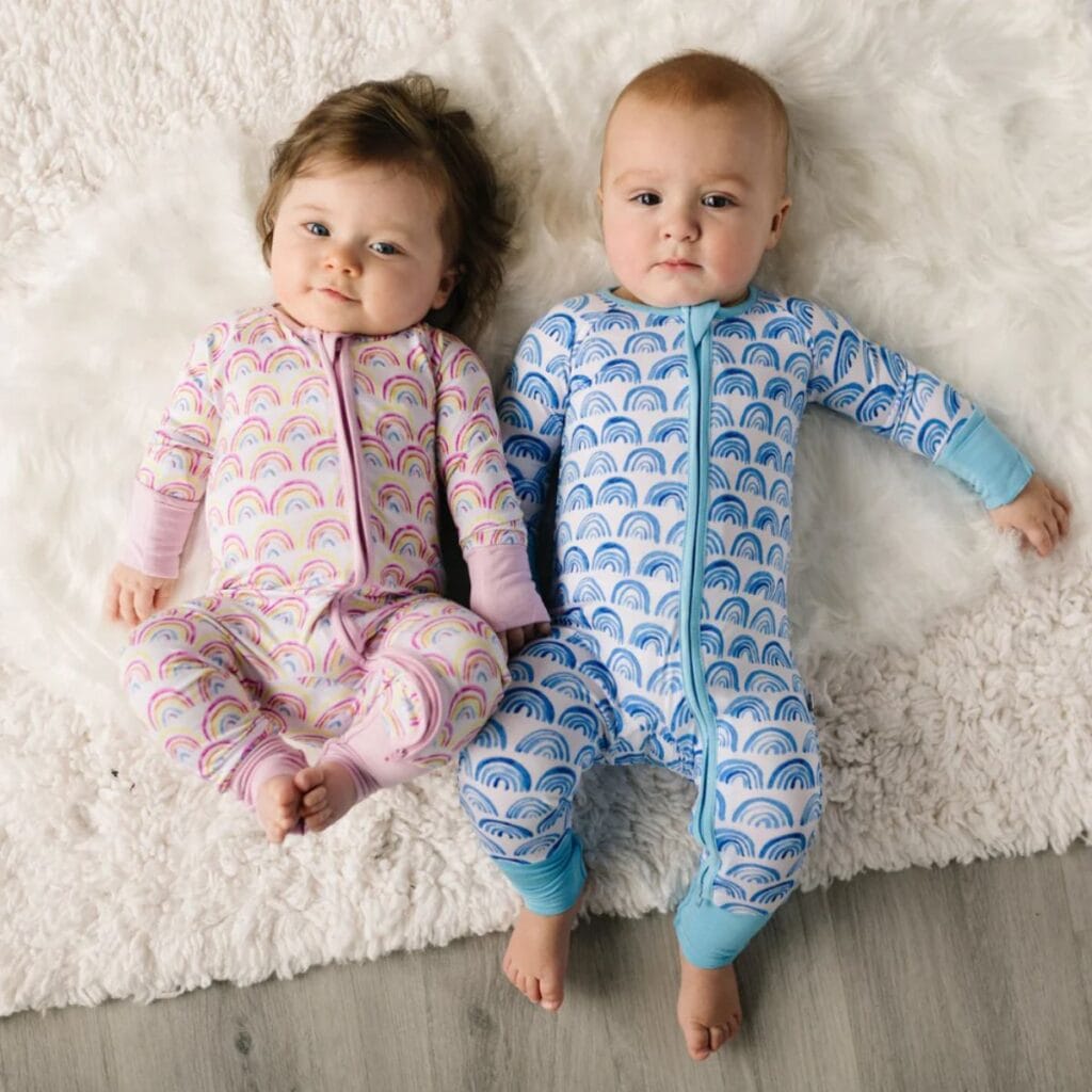 A pair of babies in rainbow pajamas. While each set of pj's has the same motif, one is in pink and the other is blue.