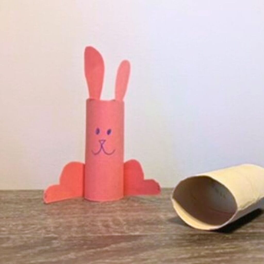 A pink bunny made with construction paper wrapped around a toilet paper roll. Its face is drawn on with a pen.