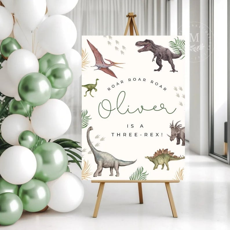 The image displays a playful birthday sign or card set on a wooden easel, surrounded by a bunch of helium balloons in white and metallic green. The sign features illustrations of dinosaurs, including a T-Rex, a Stegosaurus, and a Pterodactyl among others, in a realistic yet soft art style, interspersed with green foliage. At the top of the sign, in a repeated pattern, the word "ROAR" is printed in a hand-written style font. The main text in a script font announces "Oliver is a THREE-REX!" playing on the word "T-Rex" to celebrate what is presumably Oliver's third birthday. The artwork has a modern, cheerful feel, using a neutral white background that makes the green text and dinosaur illustrations stand out.