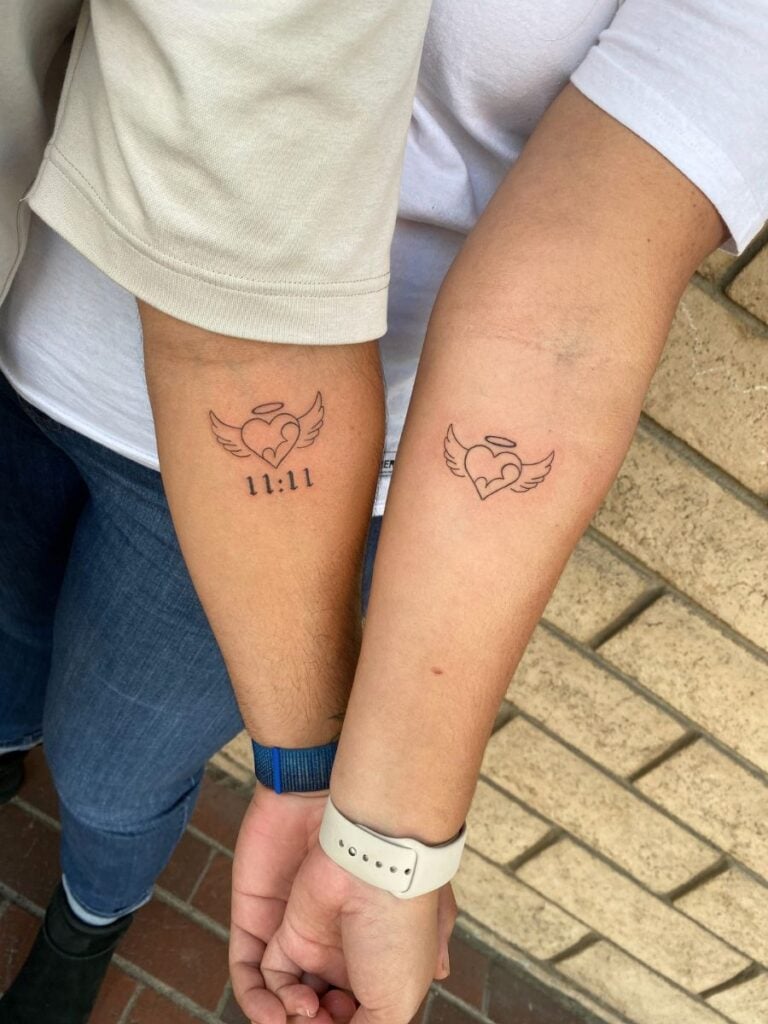 Arms of a husband and wife with matching tattoos of a heart with wings and a halo. Inside the heart is simple line art of a baby.