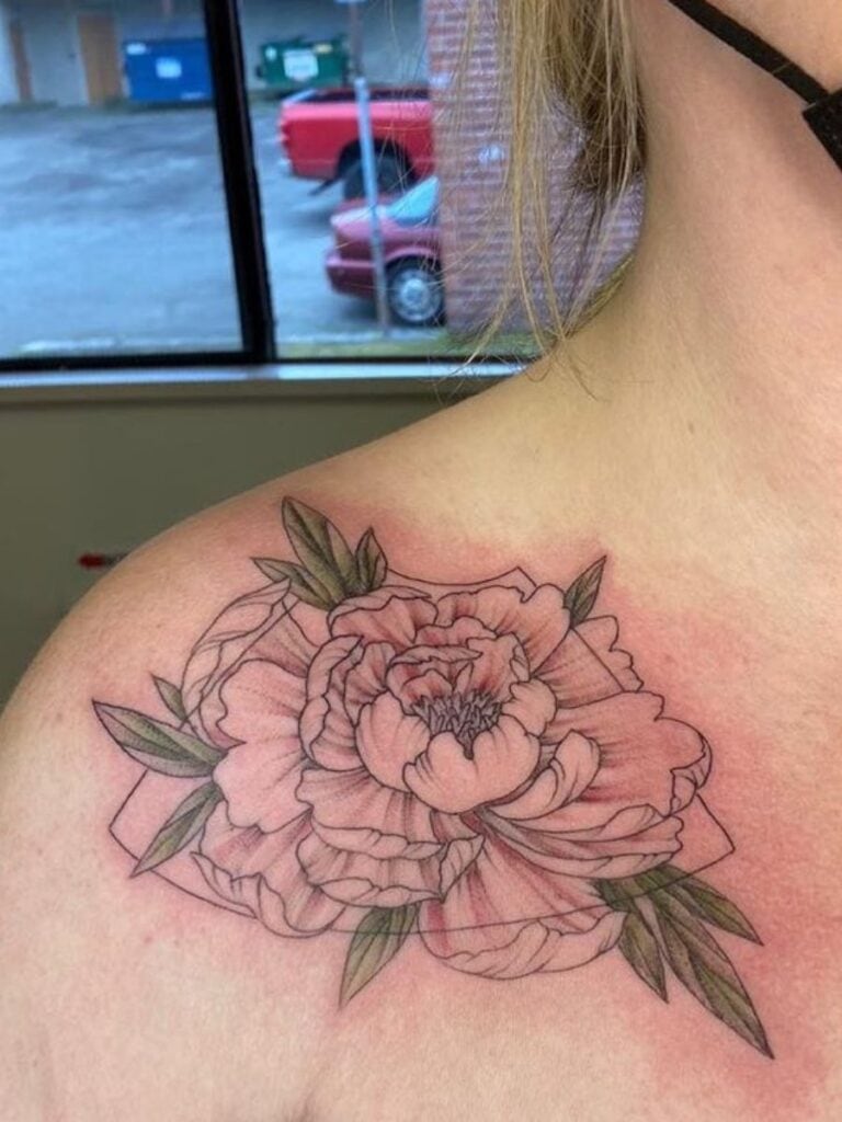 Image of a woman's shoulder with a blooming peony tattooed on it. Behind the peony is line art in. the shape of the frame of an ultrasound
