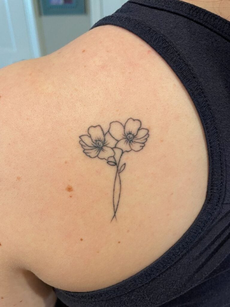 A small line art tattoo of two intertwined poppies on a mother's left shoulder.