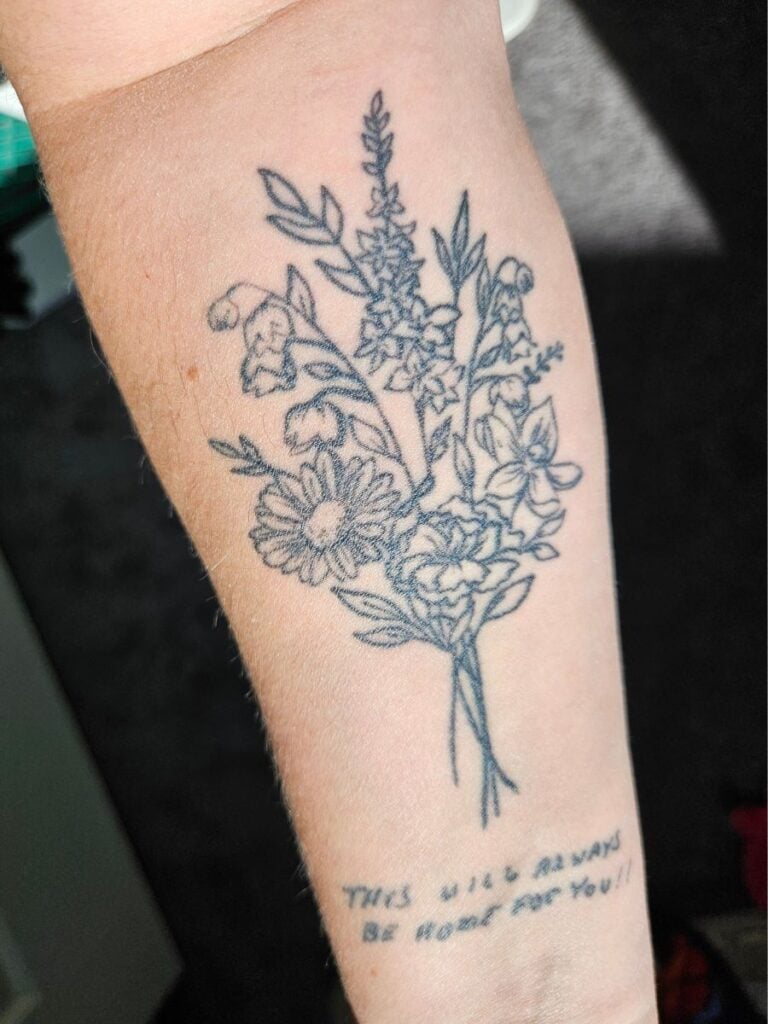 Tattoo of bouquet of several flowers, with the words "This will always be home for you!!" inked below